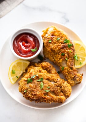 Two air fryer fried chicken pieces on a white plate with ketchup and lemon