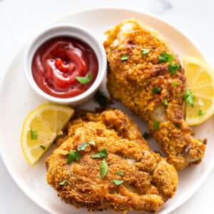 Two air fryer fried chicken pieces on a white plate with ketchup and lemon