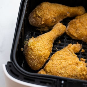 Four coated uncooked chicken pieces in an air fryer basket