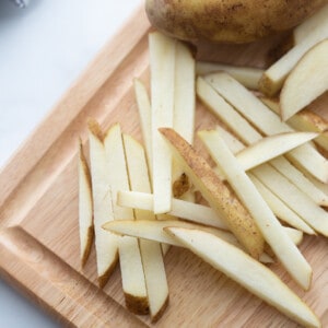 Potatoes cut into french fry slices on a wooden cutting board