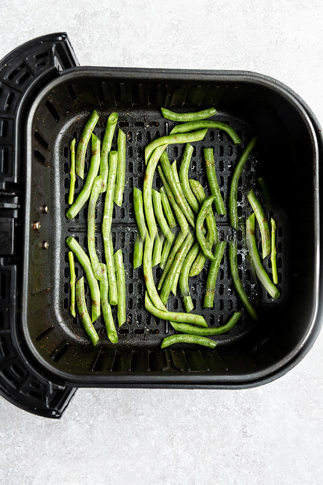 Partially cooked green beans inside of an Air Fryer basket on a kitchen countertop