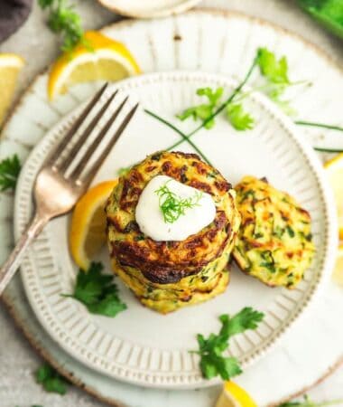 Top view of a stack of air fryer zucchini fritters on a white plate with a dollop of sour cream and dill