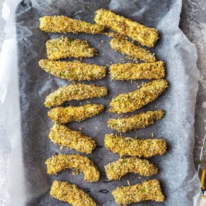 Top view of coated raw avocado fries on parchment paper on a baking sheet