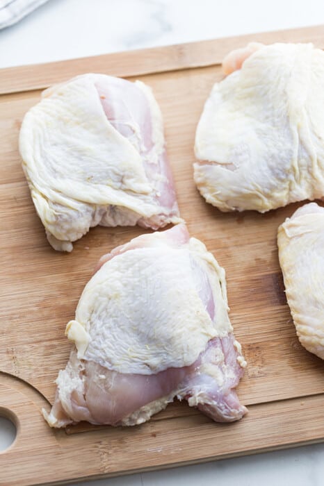 Four raw chicken thighs on a wooden cutting board