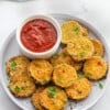 A pile of crispy zucchini chips on a white plate with a side of ketchup