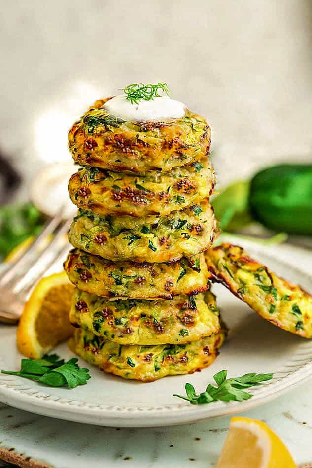 A stack of six homemade zucchini fritters with a seventh one leaning against the stack