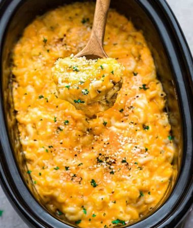 A Wooden Spoon Scooping Out a Large Bite of Mac and Cheese From a Crock Pot