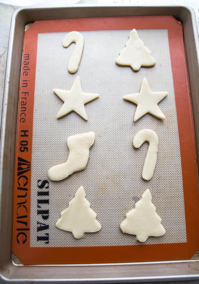 Top view of raw sugar cookie dough cut into shapes on a silicone baking mat