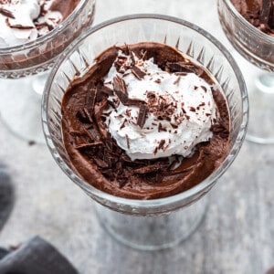 Avocado Chocolate Pudding in three glass jars with vegan whipped cream