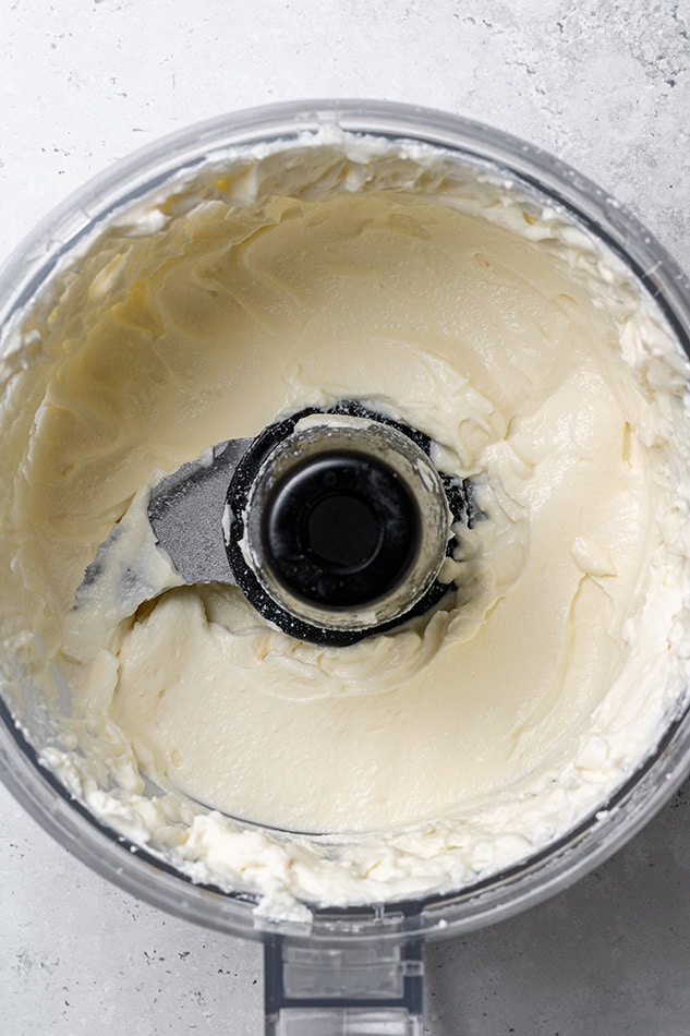 Whipped ricotta inside of a food processor on a gray surface