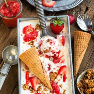 Top view of paleo ice cream in a loaf pan with an ice cream scoop and strawberries in a bowl