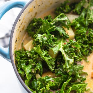 Kale, chicken broth and chopped potatoes in a blue dutch oven