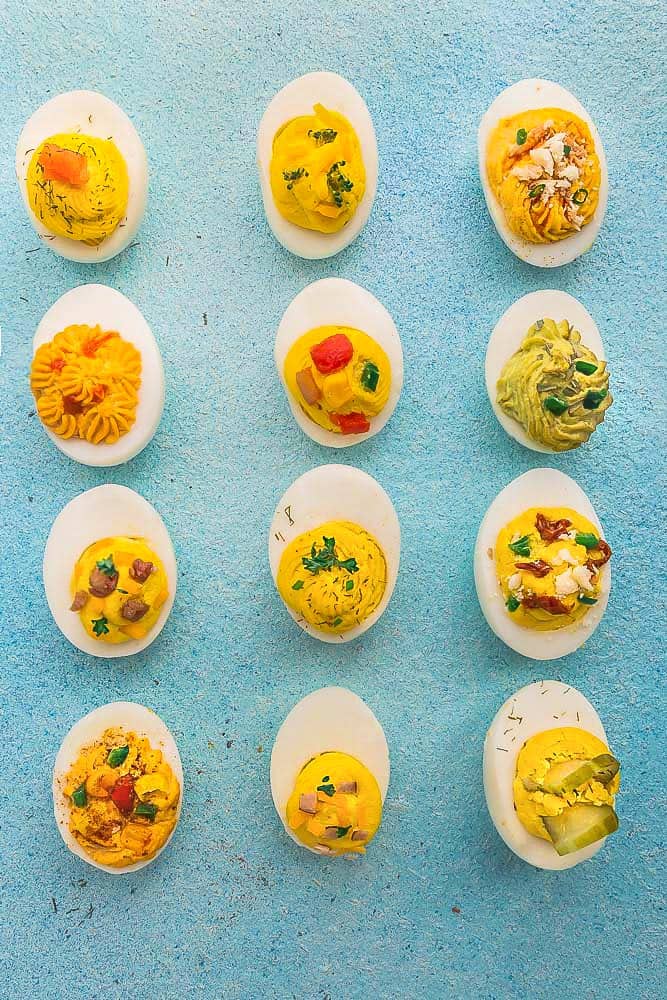 12 Various Deviled Eggs Evenly Spaced on a Blue Surface