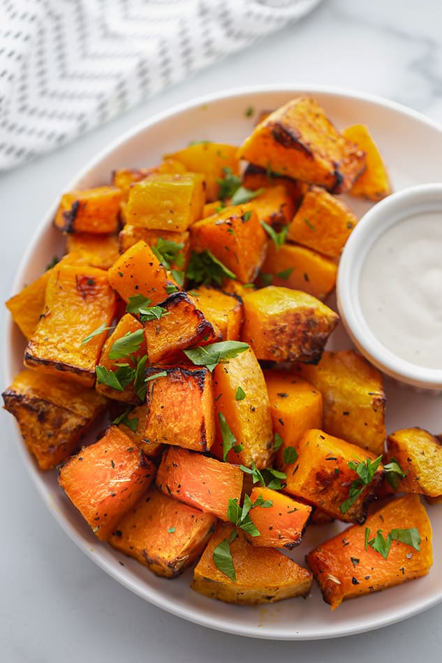 Cubes of Air Fryer butternut squash piled onto a plate on top of a marble countertop
