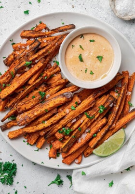 Close-up overhead shot of a pile of crispy air fryer carrot fries on a white plate with a side of dipping sauce and lemon