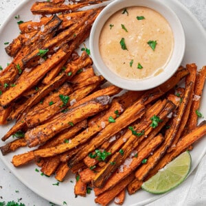 Close-up overhead shot of a pile of crispy air fryer carrot fries on a white plate with a side of dipping sauce and lemon