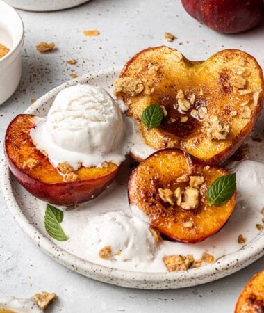 Close-up of three air fryer peach halves topped with ice cream on a white plate