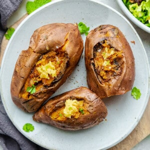 Three Instant Pot sweet potatoes with vegan butter and parsley on a white plate