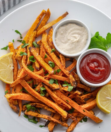 Top view of air fryer sweet potato fries on a white plate with ketchup and aioli