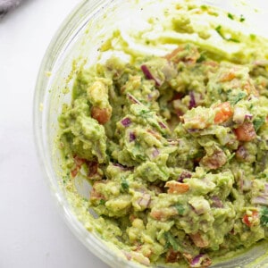 Mashed avocado, diced red onion, diced tomatoes and lime juice in a clear mixing bowl