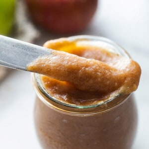 Side view of apple butter in a glass jar with a knife