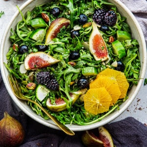 Top view of an arugula salad in a white bowl with figs + citrus