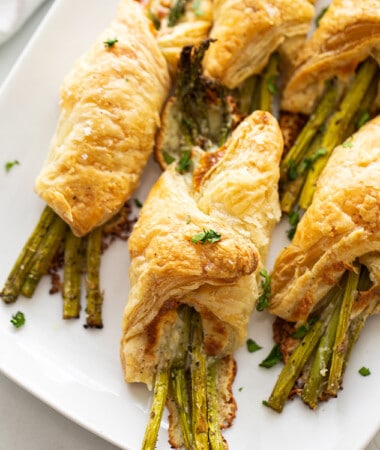 Overhead close-up shot of a bunch of 5 of baked asparagus bundles on a white rectangular platter