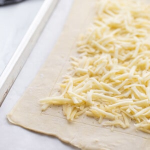 Rolled puff pastry with shredded cheese on a baking sheet