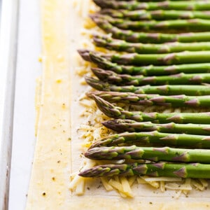 Rolled puff pastry with shredded cheese and asparagus spears on a baking sheet