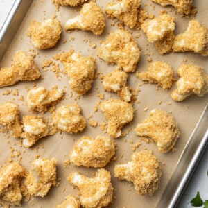 A batch of unbaked coated cauliflower wings spread out on a parchment-lined baking sheet