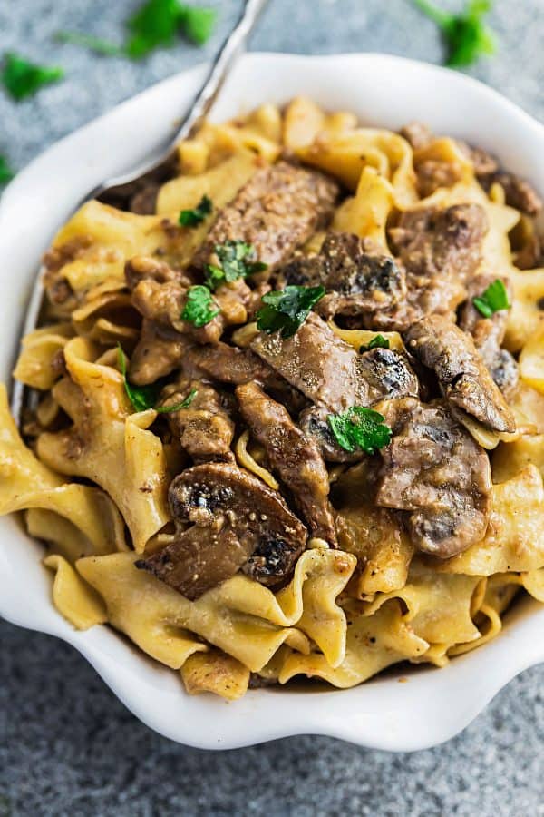 A serving of the best beef stroganoff recipe in a white serving bowl with a silver fork. 