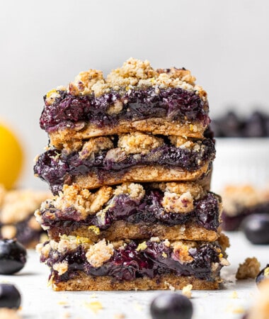 Side view of four blueberry crumb bars stacked on a white background