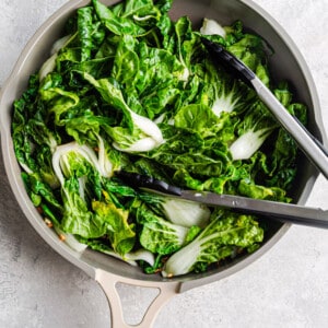 A pile of uncooked bok choy in a large wok with tongs