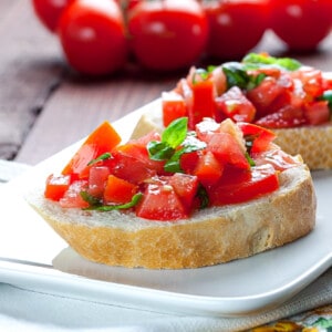 Two crostini topped with marinated tomatoes, basil and olive oil
