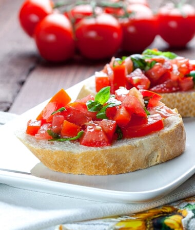 Two crostini topped with marinated tomatoes, basil and olive oil