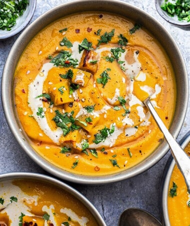 Top shot of three creamy butternut squash soup in grey bowls with a spoon