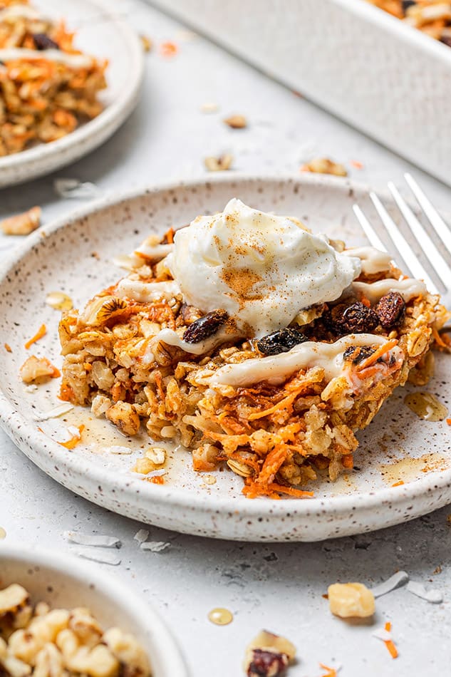 A square of carrot cake baked oatmeal topped with a dollop of dairy-free yogurt and a sprinkle of cinnamon