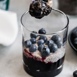 Side view of the making of one vegan chia pudding in a cup layered with blueberries and blueberry jam
