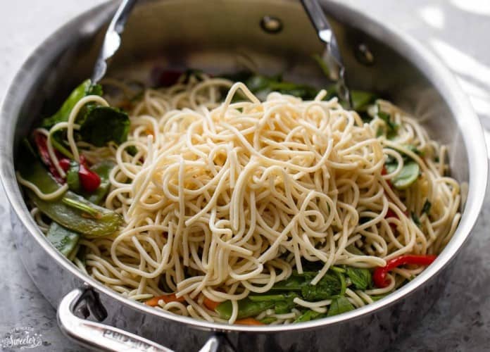 Chicken Lo Mein Noodles - the best & most authentic easy restaurant quality dish ready under 30 minutes! Perfect for busy weeknights and way better and healthier than takeout! Plus weekly meal prep and step-by-step video! Uncooked low mein noodles in a large silver skillet with spinach, red bell peppers and carotts for an easy Slow Cooker Chicken Lo Mein recipe.