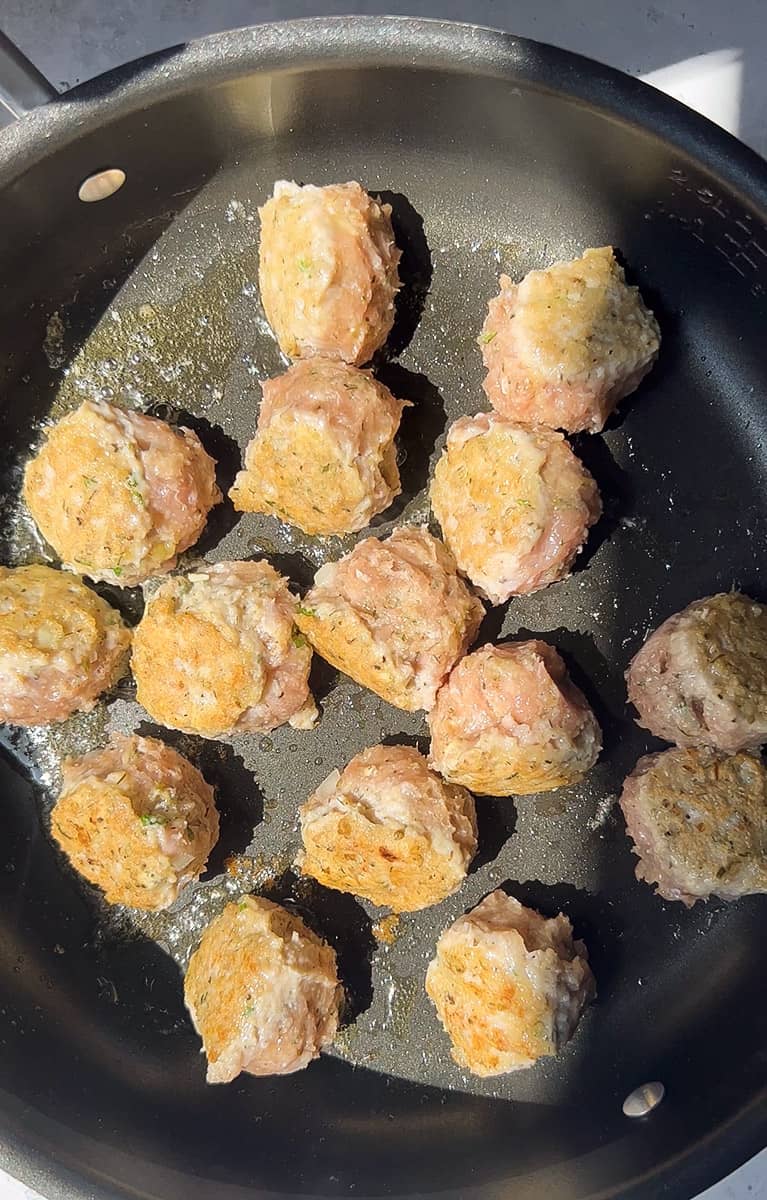 A batch of half cooked chicken meatballs in a skillet
