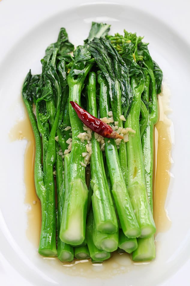 Sautéed Chinese broccoli on a white plate with a red pepper on top