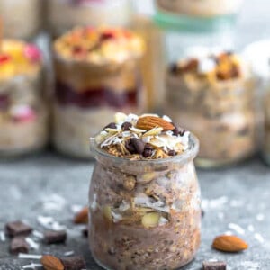 Side view of a jar of chocolate overnight oats with chopped chocolate chips, almonds and coconut on top.