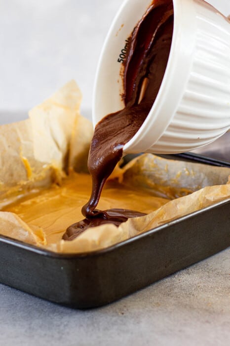 Side view of pouring melted chocolate layer in a baking pan