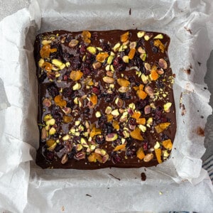 Overhead view of a parchment-lined square pan of dark chocolate bark with pistachios and dried fruit