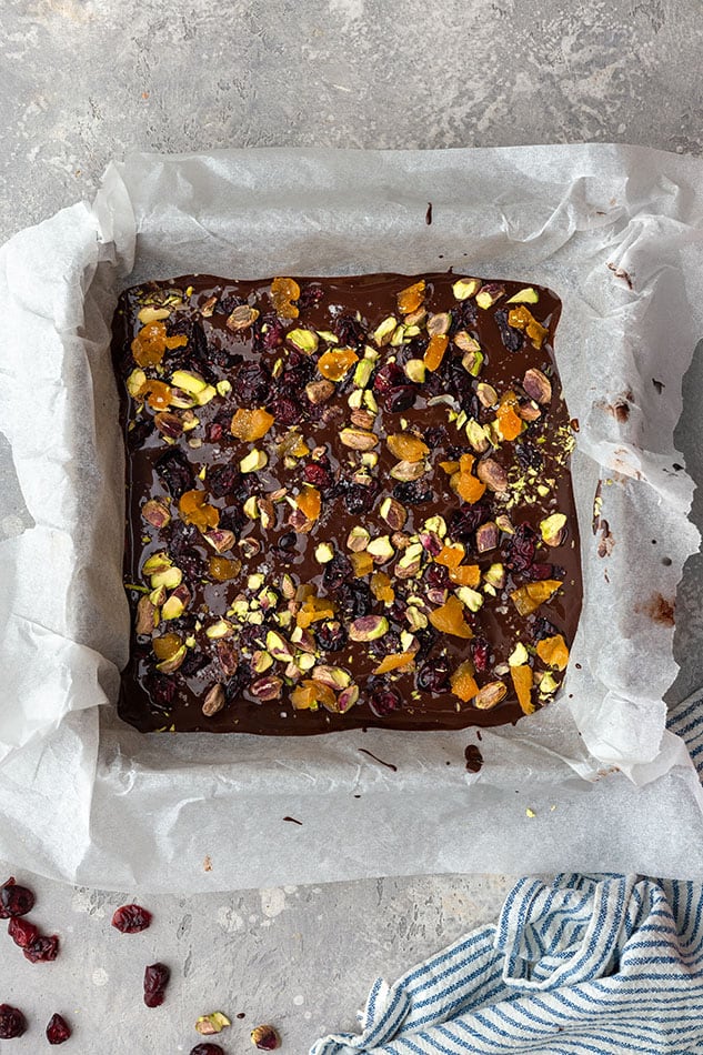 Overhead view of dark chocolate bark with pistachios and dried fruit in a lined baking dish