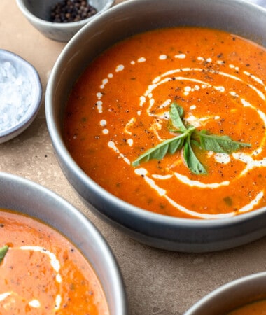 Side view of creamy tomato soup on a grey background