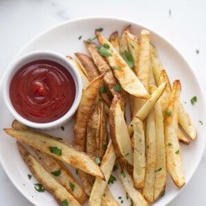 Top view of a white plate of crispy french fries with ketchup