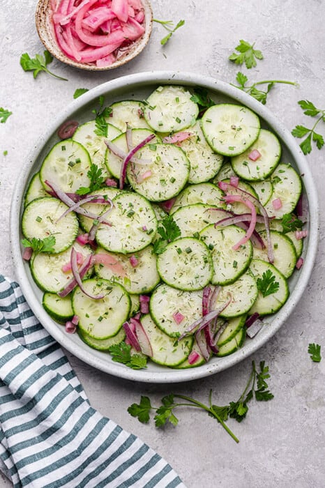 Top view of fresh cucumber salad in a white bowl with a blue striped napkin