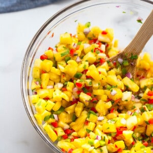 Close-up shot of a serving of fresh pineapple salsa in a clear mixing bowl with a wooden spoon