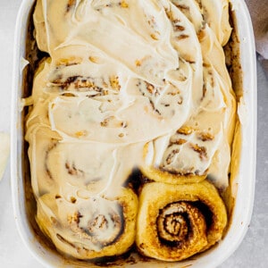 Top view of frosted dairy free pumpkin cinnamon roll dough in a white baking dish